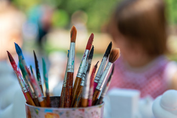 Fototapeta premium Children in the park paint with brushes and watercolors. Close-up of paintbrushes on blurred background. Image