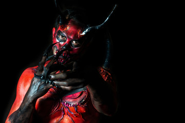 Halloween concept. Red devil or lucifer man point finger on black background. Darkness fantasy face...