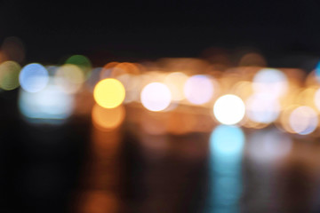 Fototapeta premium Abstract colorful blurred bokeh soft bright circle light on nightlife at river. Wallpaper and background. Defocused light night landscape with reflection on river.