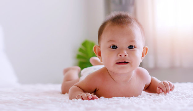 Cheerful cute baby lying and relax on white bed looking at something or family. Newborn boy wear diapers playing on the bed at home.
