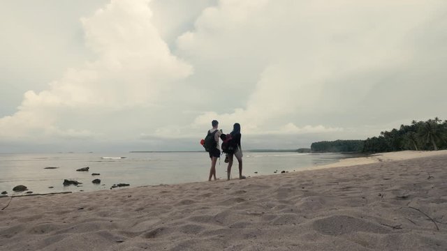 Back view of a couple backpackers walking on the beach in a tropical island.