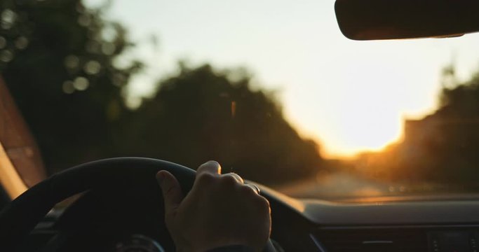 Man Driving a Car at Sunset. SLOW MOTION 4K DCi. Male Hand on steering wheel close up. Beautiful Road in blurred background.