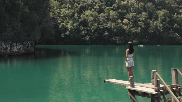 Asian girl standing on diving board watching calm nature of a lagoon.