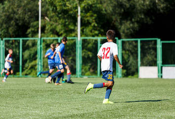 Obraz premium Boys in white and blue sportswear plays football on field, dribbles ball. Young soccer players with ball on green grass. Training, football, active lifestyle for kids concept 