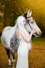 Sensual and Sexy Caucasian Blond Female with Long White Hair Standing with Horse Against Bright Light on The Background.