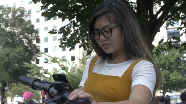 Young Woman Reserves a Scooter in the City with App