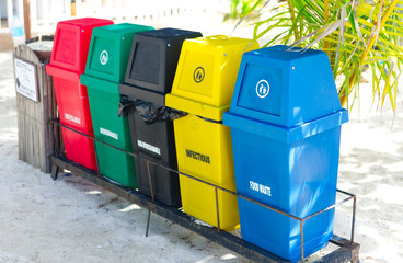 Garbage trash bins for waste segregation. Separate waste collection food waste, infection, biodegradable, non biodegradable and recycle trash bin. Multicolor trash bin on a sandy beach under coconut.