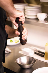 Man Chef cook salting and seasoning bowl of colorful spring salad prepared in his restaurant