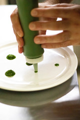 Closeup on the hand of a man chef cook setting up a plate with pesto sauce 
