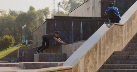 Guy does parkour on the steps, a somersault with a coup. Young men do tricks in the park. - Powered by Adobe