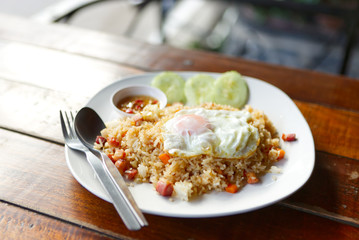 Popular Thai fried rice with pork bacon on top with sunny side up egg, garnished with sliced cucumber and chilli fish sauce .