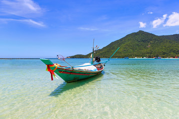 Fototapeta na wymiar Colorful traditional long tail boat floating on tropical blue turquoise crystal clear water, white sand beach and lush green mountain at Chaloklum beach in Phangan Island. Surat Thani, Gulf ofThailand