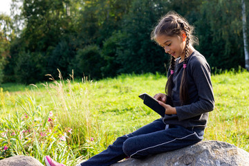 Pretty girl sitting on a stone in the fresh air with a mobile phone in her hands