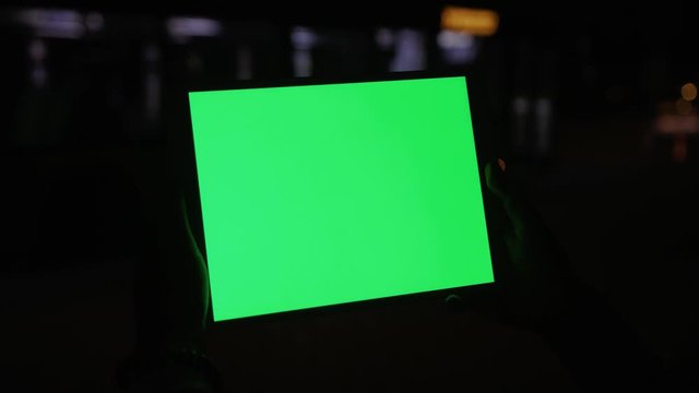 Hands of young woman holding mock-up device modern application on greenscreen display at night. Technology and people.
