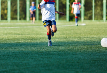 Obraz premium Boys in white and blue sportswear plays football on field, dribbles ball. Young soccer players with ball on green grass. Training, football, active lifestyle for kids concept 