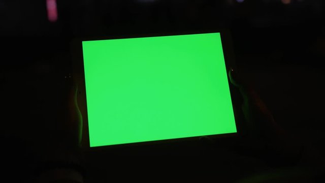 Person using digital tablet computer with bright mock-up chrome key technology green screen at dark night in the city. Close-up.