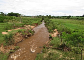 Rural river with turbid waters flowing through farmland, lacking riparian vegetation, highlighting...