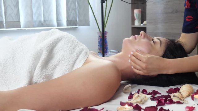 Masseur hand massaging womans's face on bed with rose petals and candle during treatment. Spa skin and body care. Facial beauty treatment. Cosmetology concept. Luxury treatment at spa salon