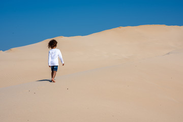 Young boy walking alone up a sand dune