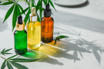 Different glass bottles with CBD OIL, THC tincture and cannabis leaves on yellow background. Flat...