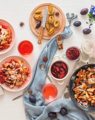 Kaiserschmarrn, Imperial pancake, traditional dessert of Austrian cuisine. White wooden table with pancakes, plum compote, fresh plums and pitcher with glasses of hibiscus tea.