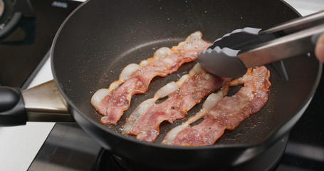 Fry bacon in pan in kitchen for breakfast