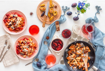 Kaiserschmarrn, Imperial pancake, traditional dessert of Austrian cuisine. White wooden table with pancakes, plum compote, fresh plums and pitcher with glasses of hibiscus tea.