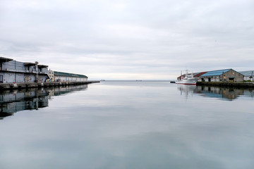 Obraz premium Harbor surrounding of fishing industry warehouse or fishery,boat is mooring on the bay floating on still water on white line skyin the port of Otaru sea on a background at Sapporo of Hokkaido in Japan