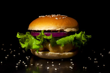 Fast food concept: Burger with cutlet, cheese, onions and lettuce on a black background