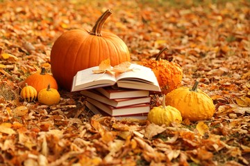 Autumn books. Reading books about autumn.Halloween books. Stack of books and  pumpkins set on autumn foliage on blurred nature background