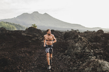Young athletic man with beard trail running fast outdoors. Topless body and chest heart rate...