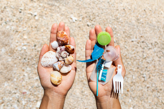 Concept of choice: save nature or continue to use disposable plastic. One hand holding beautiful shells, in the other - plastic waste. Beach sand on background. Environmental pollution problem.