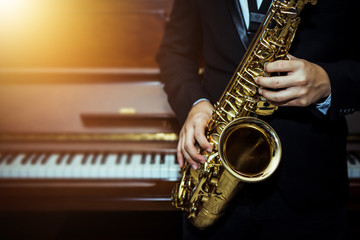 Close up of a man hand hold and playing saxophone over piano with light effected, music poster...