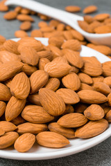 Almonds in white dish with spoon on table.