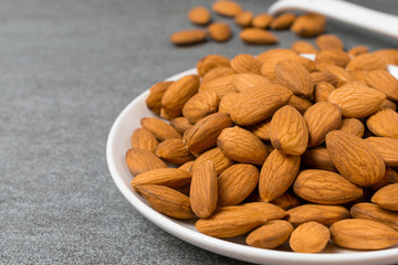 Almonds in white dish with spoon on table.