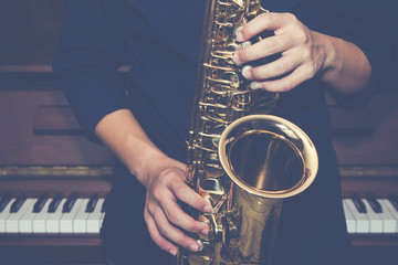 Close up of a man hand hold and playing saxophone over piano with light effected, music poster...