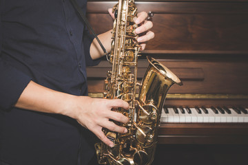 Saxophone Player hands  playing alto sax musical instrument over piano  background  ,  closeup with copy space,  can be used for music background