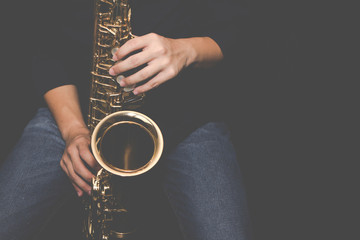 Close up of a young musician  man hands hold and playing  saxophone on black background with copy...