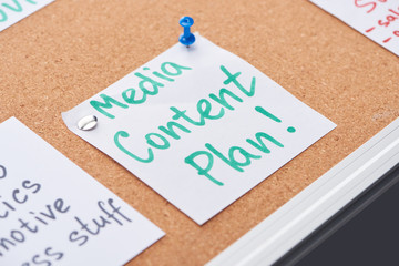 paper card with media content plan lettering pinned on cork office board