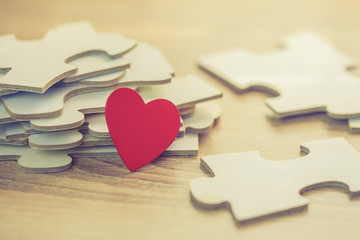 Close up of red heart over pile of jigsaws on wooden table, Conceptual image show most important part of human life is love