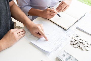 couple working saving account book and calculating her monthly expenses on calculator to calculate financial data, filling in individual income tax return.
