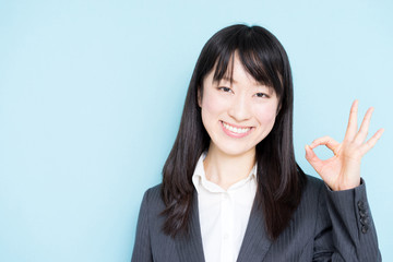 Young business woman showing OK sign against light blue background