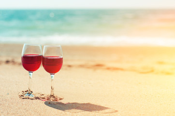Two wine glasses with red wine on the sand of the beach at the sea shore. Romantic couple.