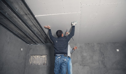 Workers fitting panel into frame of ceiling.