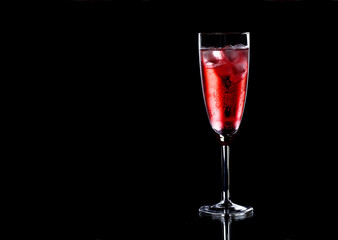 Glass of red champagne with ice on black background