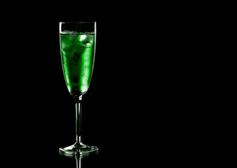 Glass of green champagne with ice on black background