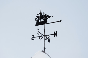 weathervane ship on the roof of the house. Against the blue sky.