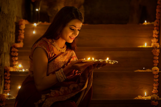 young woman sitting on stairs with diyas in hand	