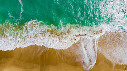Obraz premium Top view of the beautiful sandy beach with turquoise sea water. Aerial drone shot at the big ocean waves on the West coast. a deserted beach for travel and recreation