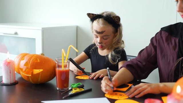 Little Girl with Mom Making Halloween Decorations. They Drawing Scary Faces on Circle Sheets of Paper. Holidays and Halloween Decorations Concept